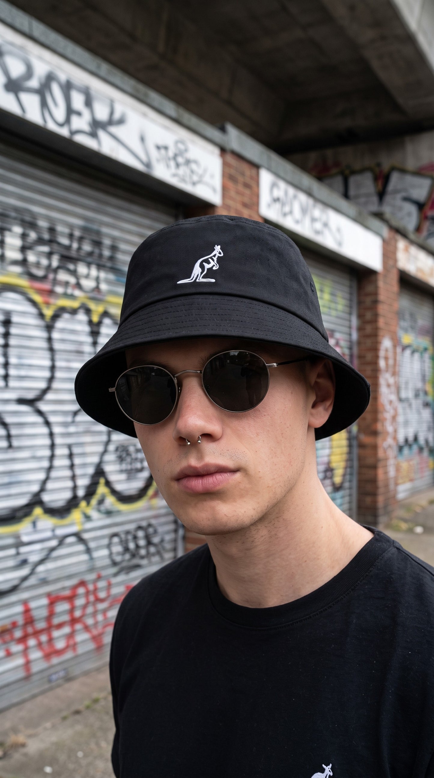 Modello con bucket hat nero GABBERPLANET in cotone con logo Australian ricamato bianco, stile urban con occhiali da sole